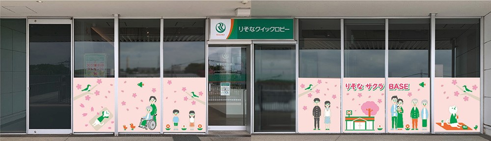 外観の下半分の窓ガラスに桜のイラストが横一面に描かれており、その中にはりそにゃや子供、子供を抱えた家族のイラストなども描かれている写真