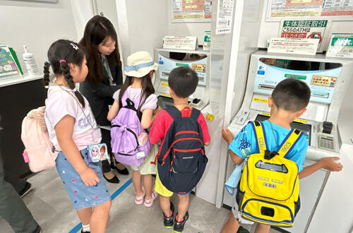 子ども達が銀行内の見学でATMの説明を受けている様子